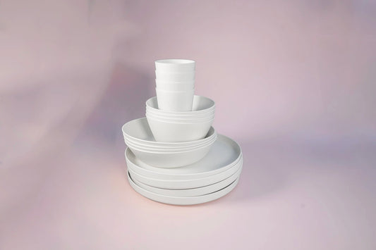A stack of matte white ceramic tableware, including plates and bowls, arranged on a soft pink studio background.