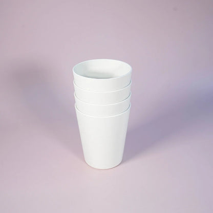 A stack of four plain white tapered cups or small bowls standing upright on a soft lavender-pink studio background.