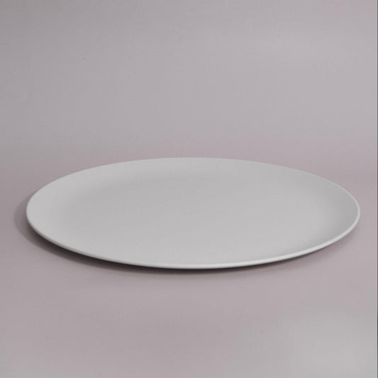 A minimalist white oval ceramic plate with a shallow rim, photographed against a seamless light gray studio background.