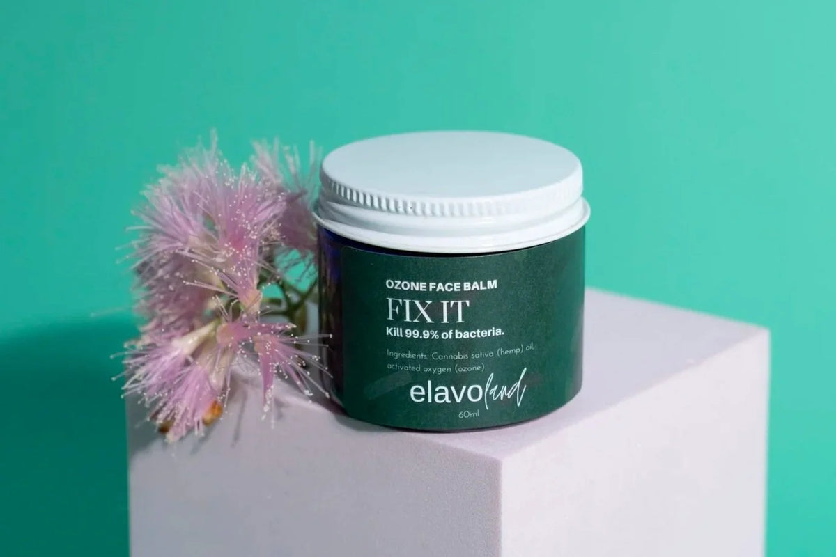 Hemp ozone face balm container with white lid, green label, placed on pink block with pink flower, natural skincare product