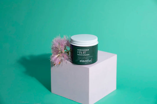 Hemp ozone face balm container with white lid, green label, placed on white block with pink flower, natural skincare product