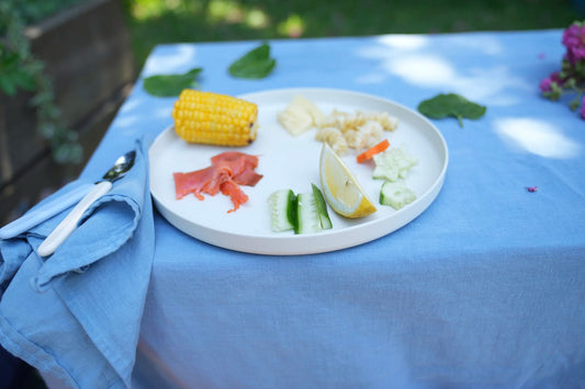 A white oval plate with a colorful assortment of small vegetables and a lemon wedge, set on a light blue tablecloth outdoors.
