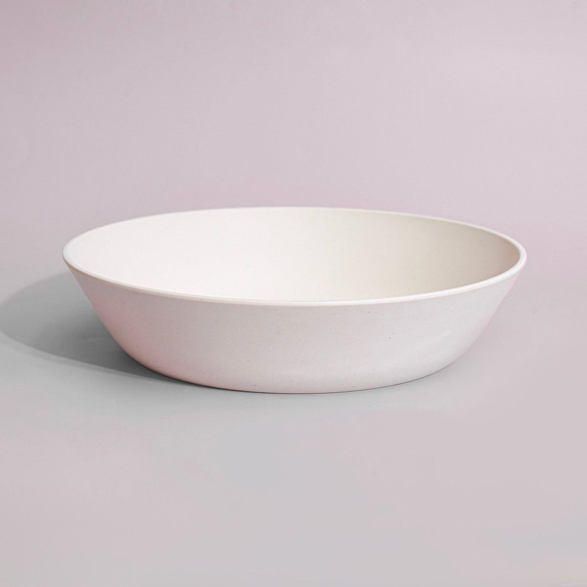 A minimalist white ceramic bowl with a wide, shallow profile, photographed against a solid light gray background.