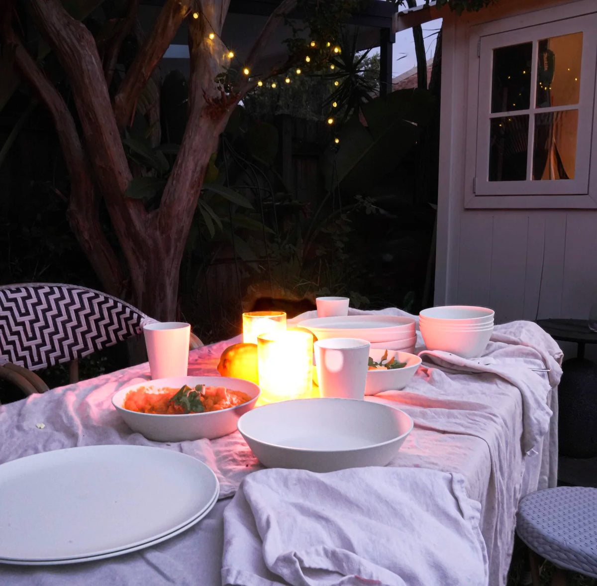 outdoor dinner table in candlelight with white bowls and plates