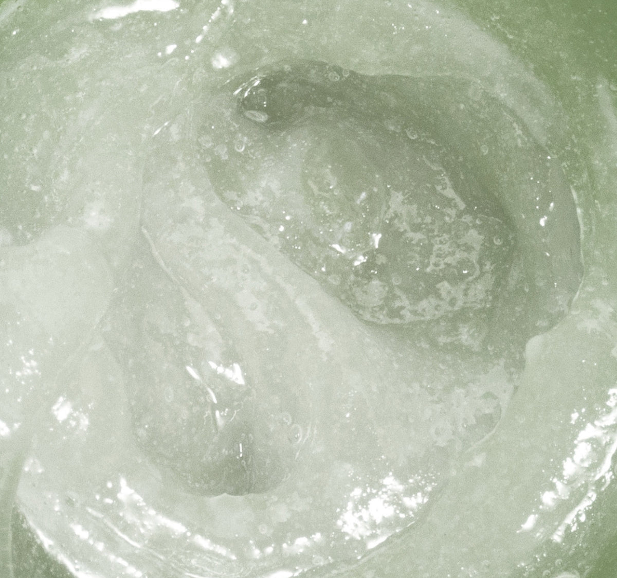 A close-up texture shot of a translucent, milky white gel or wax with a soft, cloudy sheen and subtle greenish tint.