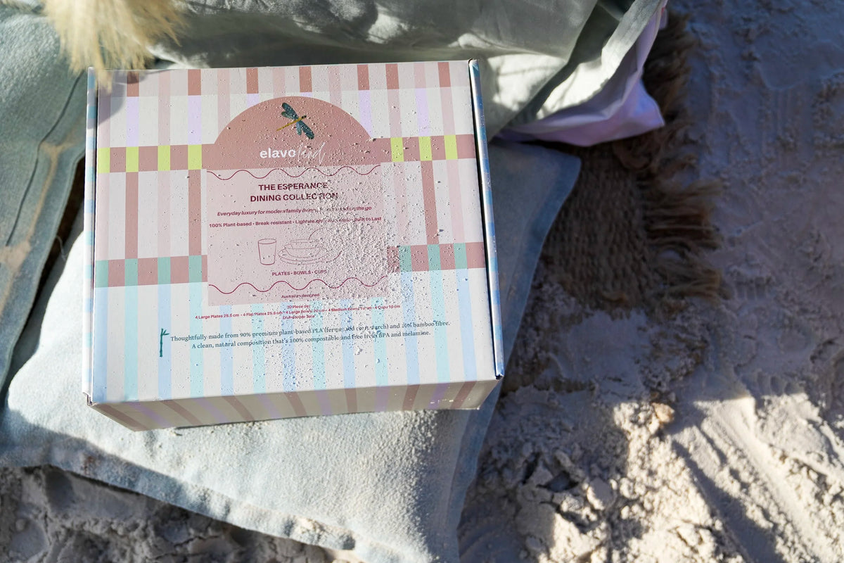 A boxed product labeled 'elavo' and 'The Experience' placed on a light blue blanket outdoors on sandy ground.