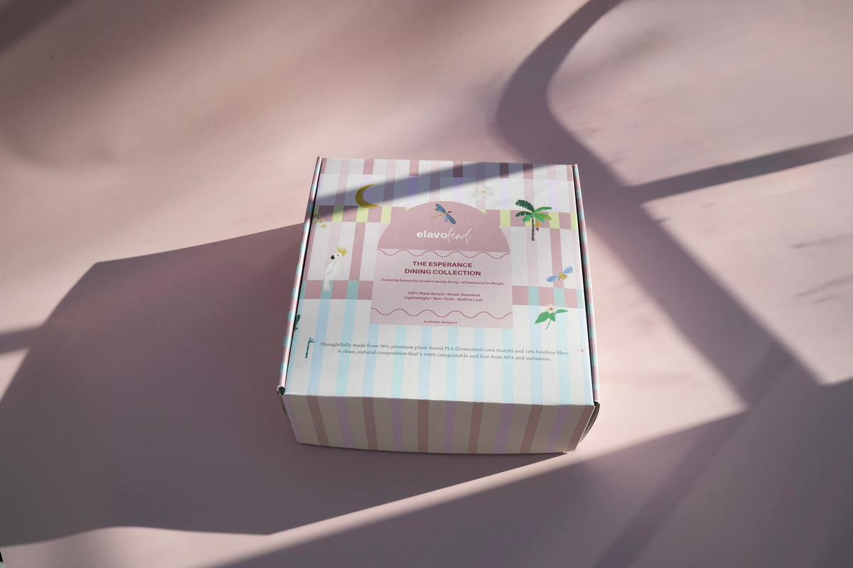 A pastel striped product box with tropical illustrations, photographed on a light surface with strong diagonal shadows.