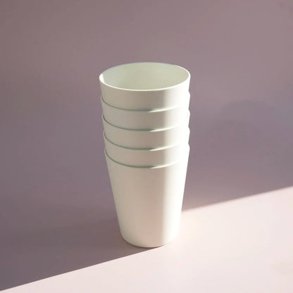 A stack of four matte white tapered cups with subtle mint green horizontal stripes near the rims, standing on a light surface against a soft lavender-gray background.