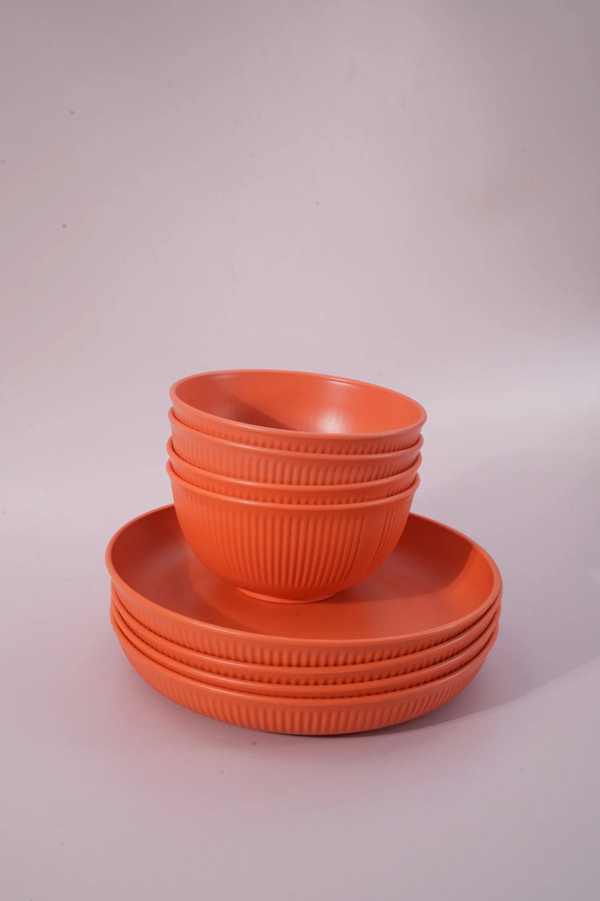 A set of orange plastic bowls and plates with a ribbed texture, stacked neatly on a light gray studio background.