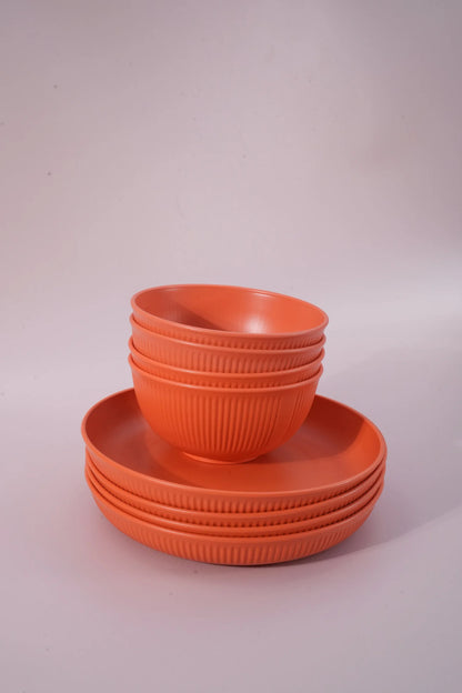 A set of orange plastic bowls and plates with a ribbed texture, stacked neatly on a light gray studio background.