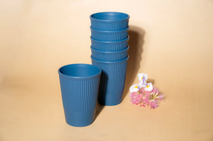 A set of five blue ribbed plastic cups, with four stacked and one standing in front, displayed on a beige background next to a small decorative flower.