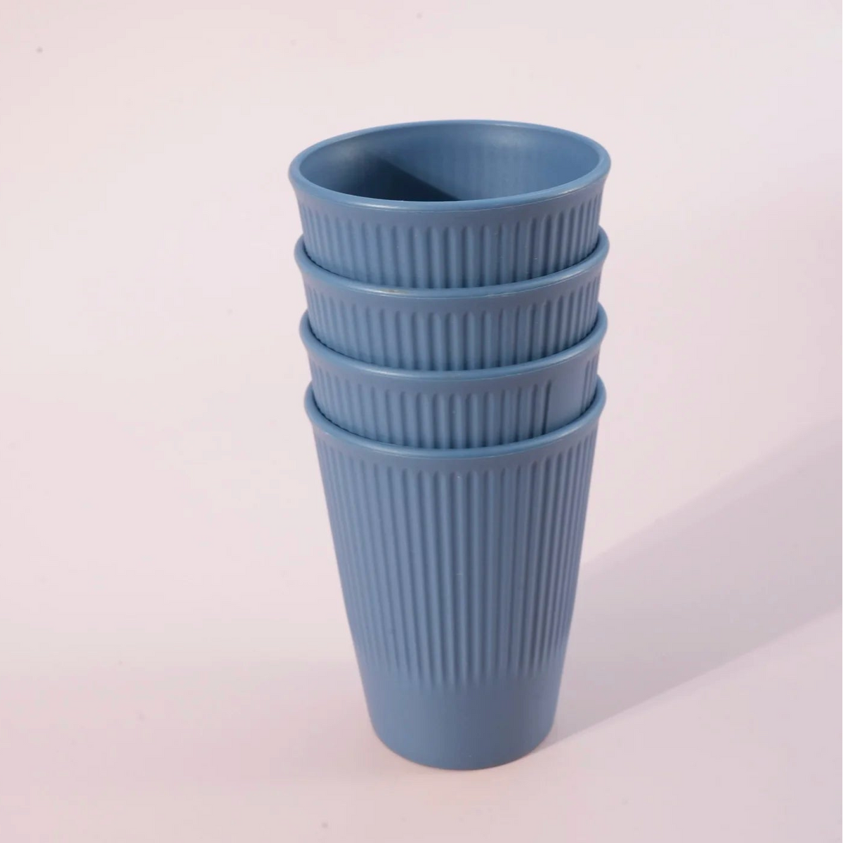 A stack of four ribbed plastic cups in a dusty light blue color, standing on a light pinkish-white background.