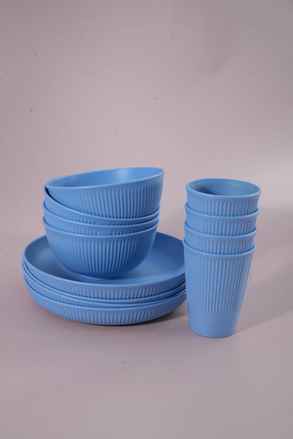 A set of light blue ribbed dinnerware, including bowls, plates, and cups, arranged on a neutral light gray background.