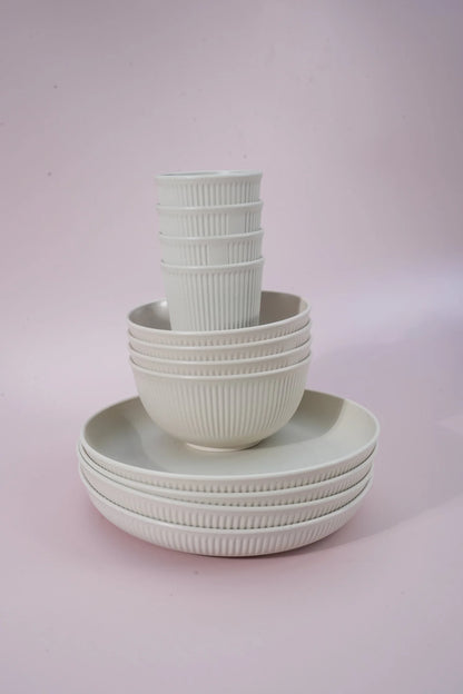 A set of ribbed ceramic tableware, including bowls and plates, stacked neatly on a soft pink studio background.