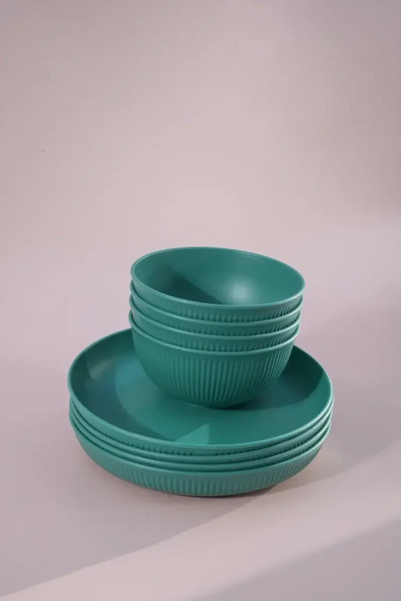 A set of teal green ribbed bowls and matching plates stacked together on a light gray studio background.