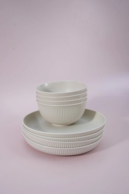 A set of white ribbed ceramic bowls and plates stacked neatly on a soft pink studio background.
