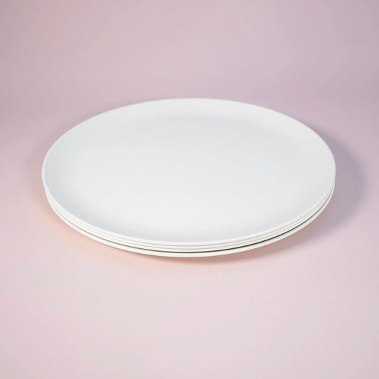 A stack of four plain white ceramic plates photographed on a soft pink studio background.