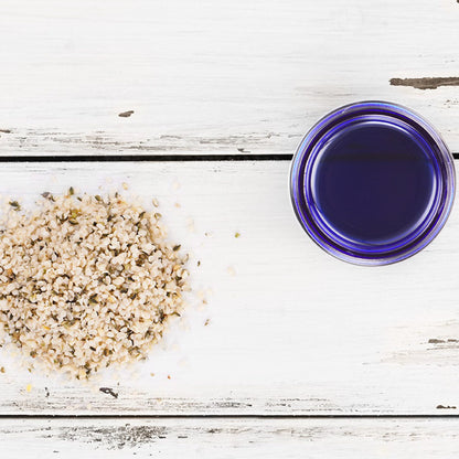 White wooden surface with hemp seeds and a blue glass jar of ozone face balm, natural ingredients for skincare