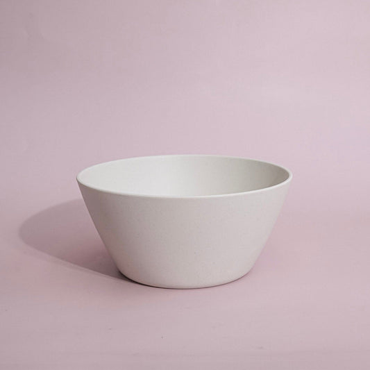A minimalist white ceramic bowl with a wide, gently sloping rim, set against a solid light pink background.