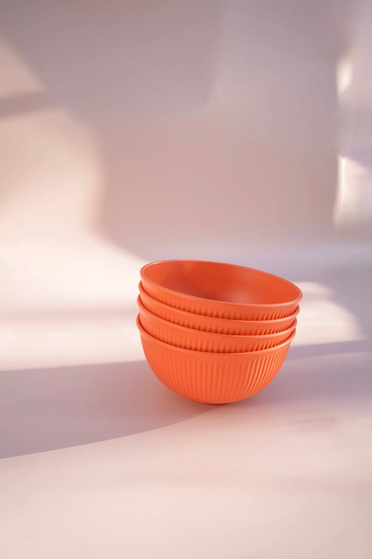 A stack of four ribbed orange bowls on a warm, light beige surface with soft shadows.