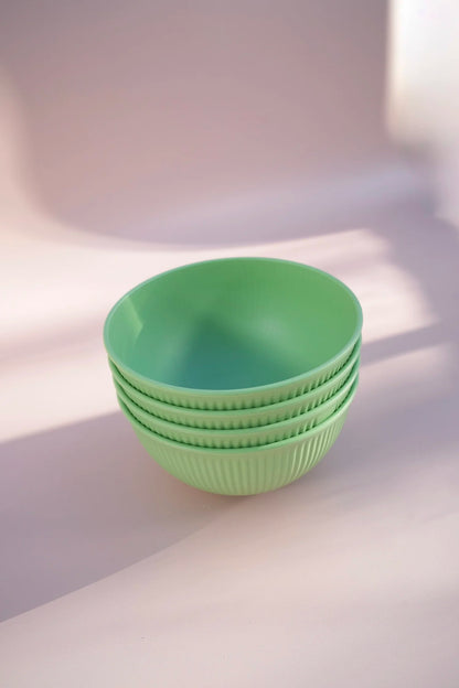 A stack of four light green ribbed bowls with a smooth interior, set against a soft pinkish-beige background with artistic shadows.