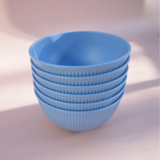 A stack of five light blue plastic bowls with a ribbed exterior and smooth interior, set against a soft pinkish-beige background with warm shadows.
