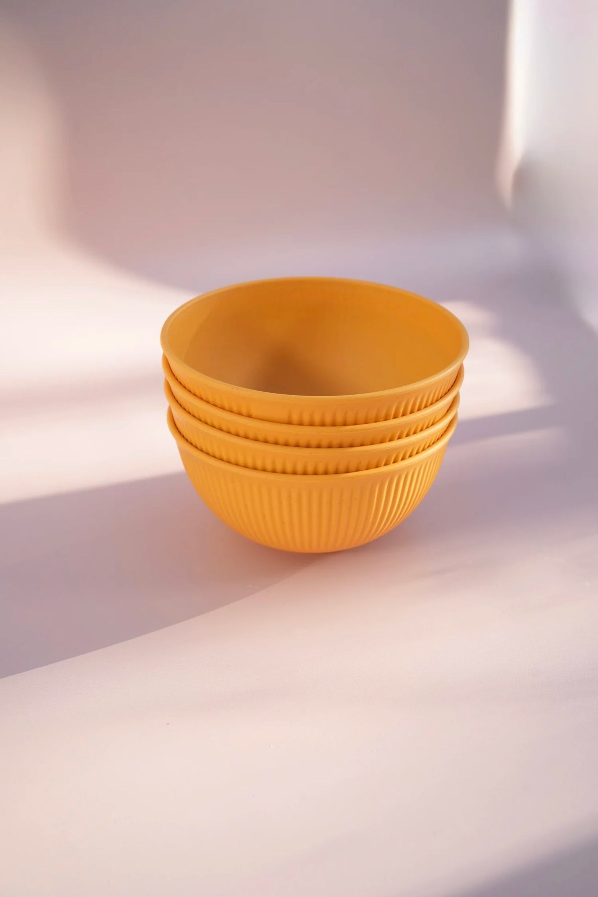 A stack of four small ribbed yellow bowls on a softly lit cream-colored surface with warm shadows.